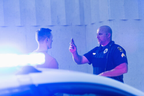 Police officer giving a sobriety test to a young man who he suspects is driving under the influence of drugs or alcohol. Police cruiser is out of focus in the foreground.