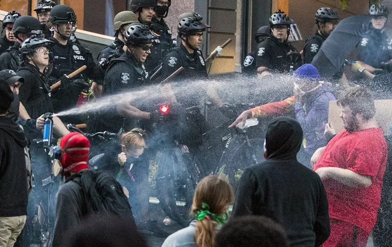 A police officer sprays a protestor with a hose during a confrontation with police.