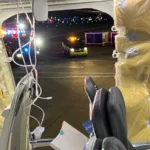 A view from an open airplane door shows a vehicle on the tarmac at night.