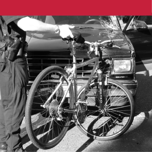 "Police officer holds damaged bicycle after collision with black pickup truck"