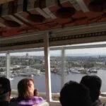 Passengers on a duck tour vehicle look out the window at a city harbor view.