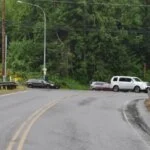 The scene of a car accident on a curving, wet road in a wooded area.