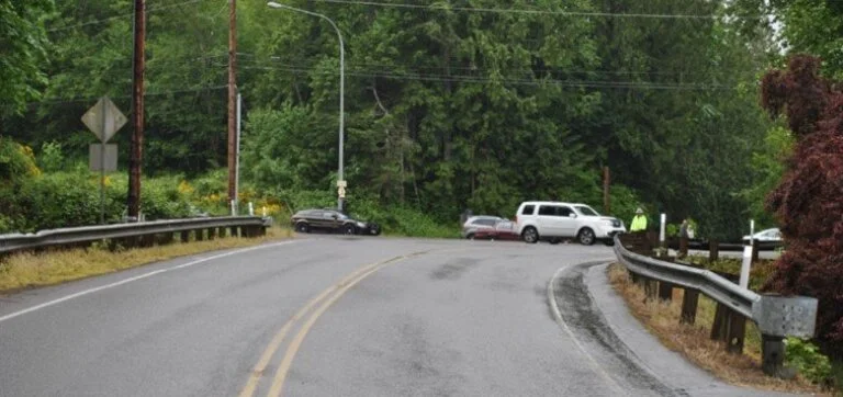 The scene of a car accident on a curving, wet road in a wooded area.