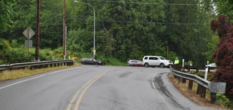 The scene of a car accident on a curving, wet road in a wooded area.
