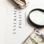 An auto insurance policy with a magnifying glass, a toy car, and hundred-dollar bills.
