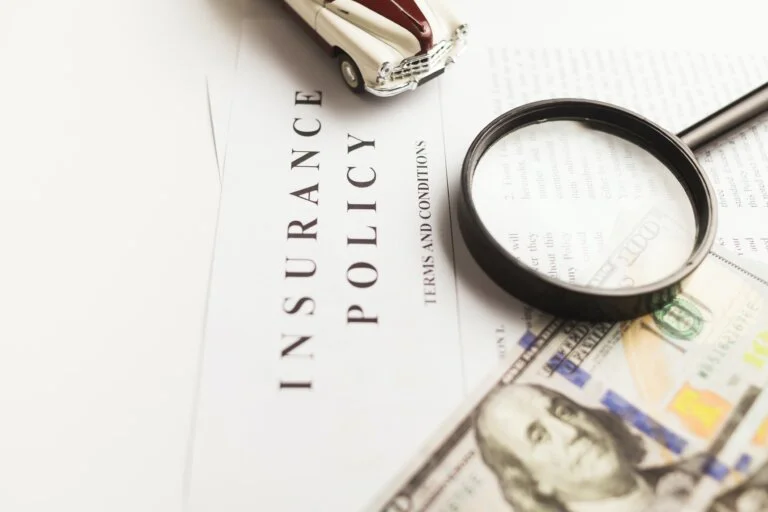 An auto insurance policy with a magnifying glass, a toy car, and hundred-dollar bills.
