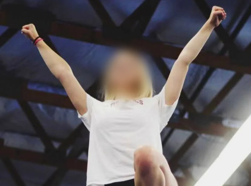 A cheerleader with a blurred-out face strikes a triumphant pose with her arms raised.