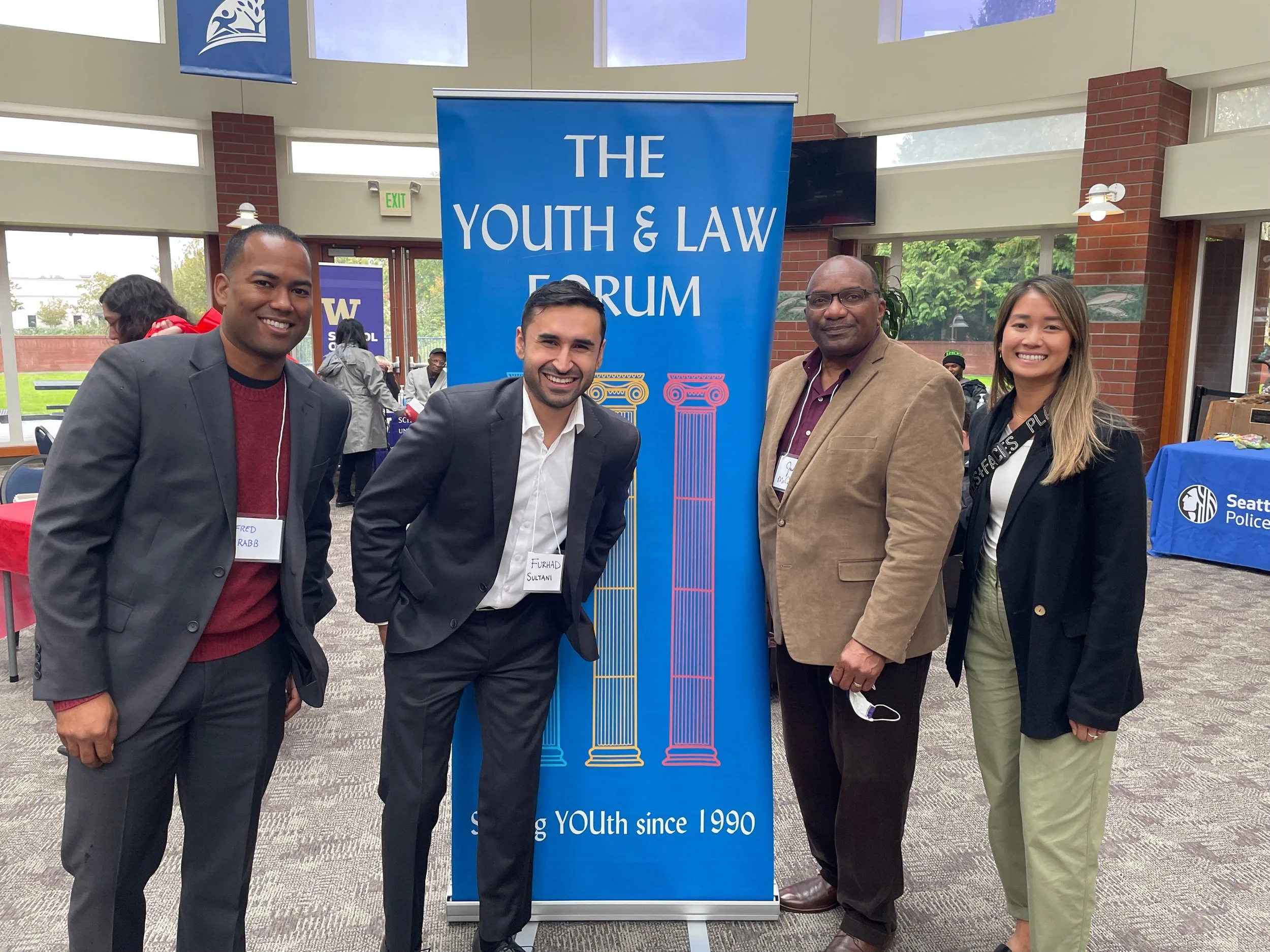 A group of four attendees poses next to "The Youth & Law Forum" event banner.