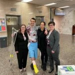 A man with a leg cast and crutches poses with three women in a courthouse lobby.