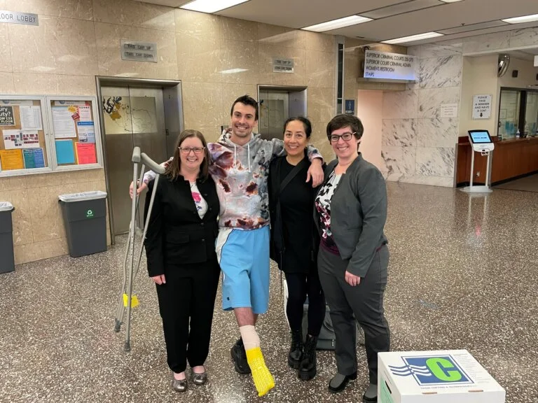 A man with a leg cast and crutches poses with three women in a courthouse lobby.