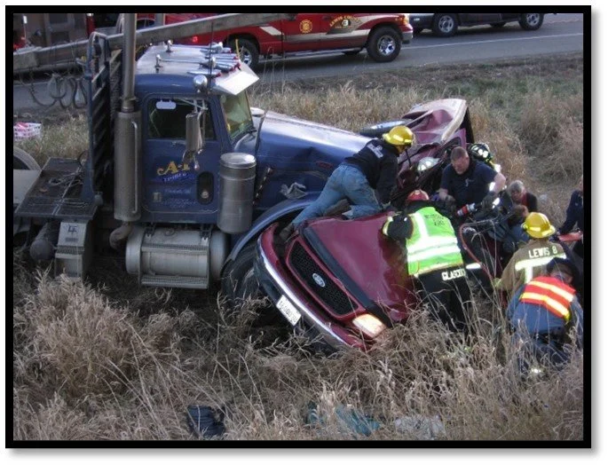 Firefighters work to rescue someone from a pickup truck crushed by a large semi-truck.