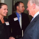 "Two people smiling and shaking hands at a formal event"
