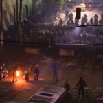 A confrontation at night between a large crowd and a small group with torches in a street.