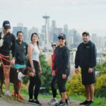 "Group of six people and a dog posing on a hill with the Seattle skyline in the background"