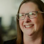 "Smiling woman with glasses in softly lit office setting"