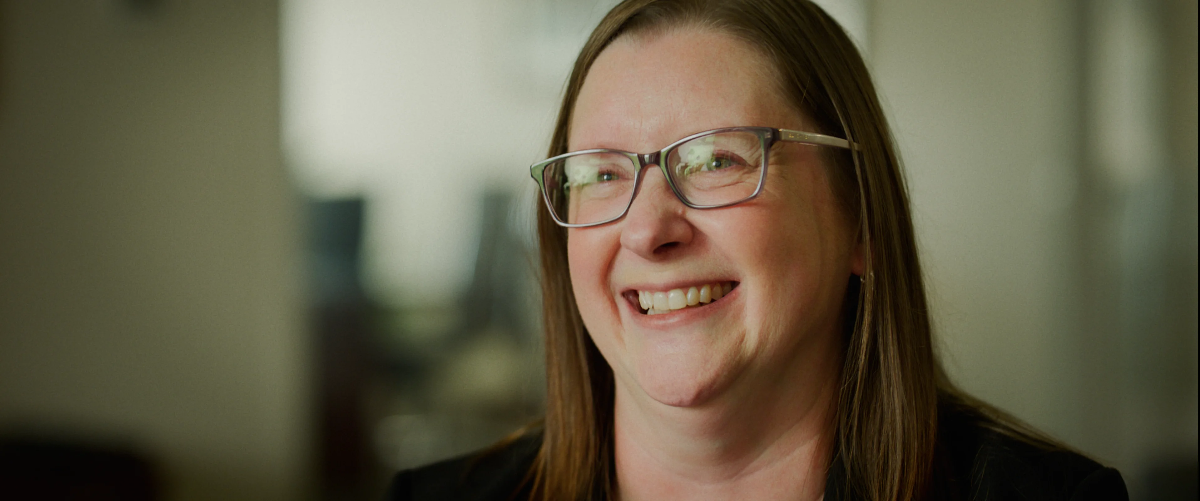 "Smiling woman with glasses in softly lit office setting"