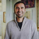 "Smiling man in beige sweater standing in decorated office"