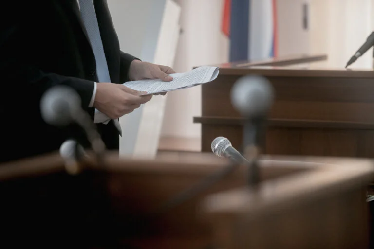 A man in a suit stands at a podium holding papers to give a speech.