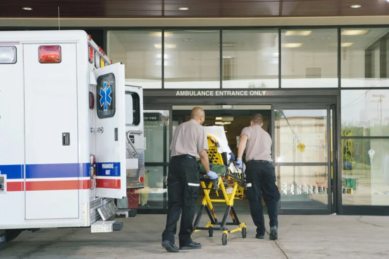 Two paramedics push a stretcher with a patient toward an ambulance entrance.