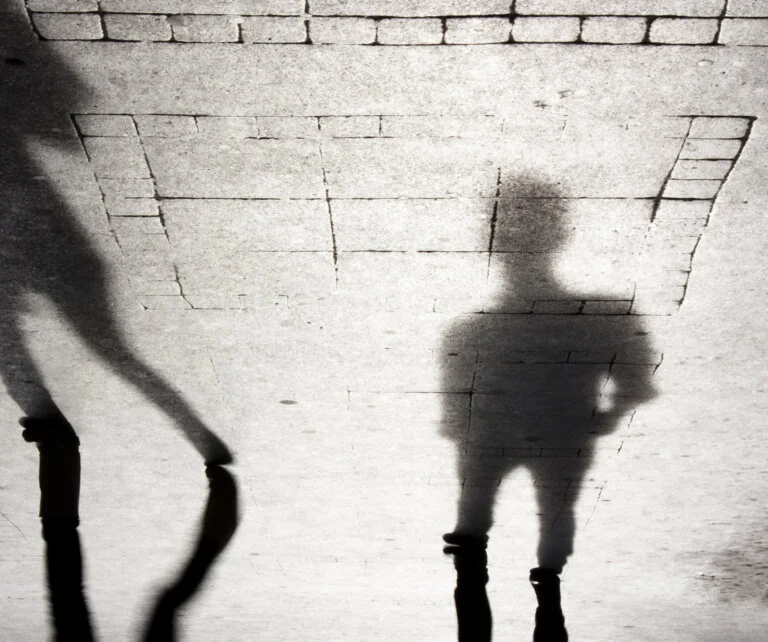 The long shadows of two people are cast on a tiled ground.