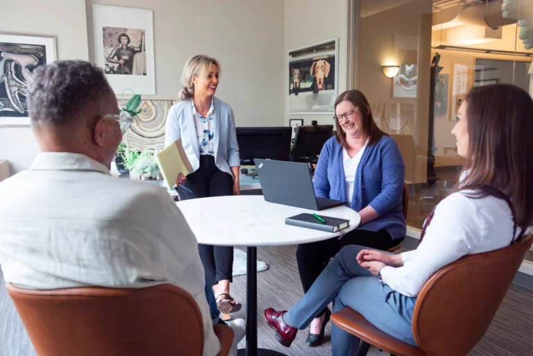 Team meeting with four professionals smiling around a round table.