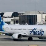 An Alaska Airlines passenger jet on the tarmac at an airport terminal.