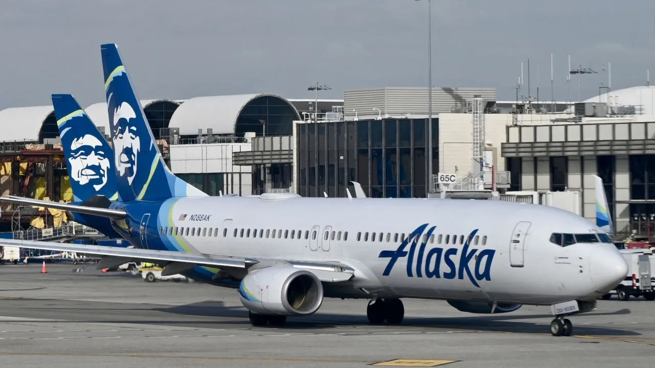 An Alaska Airlines passenger jet on the tarmac at an airport terminal.
