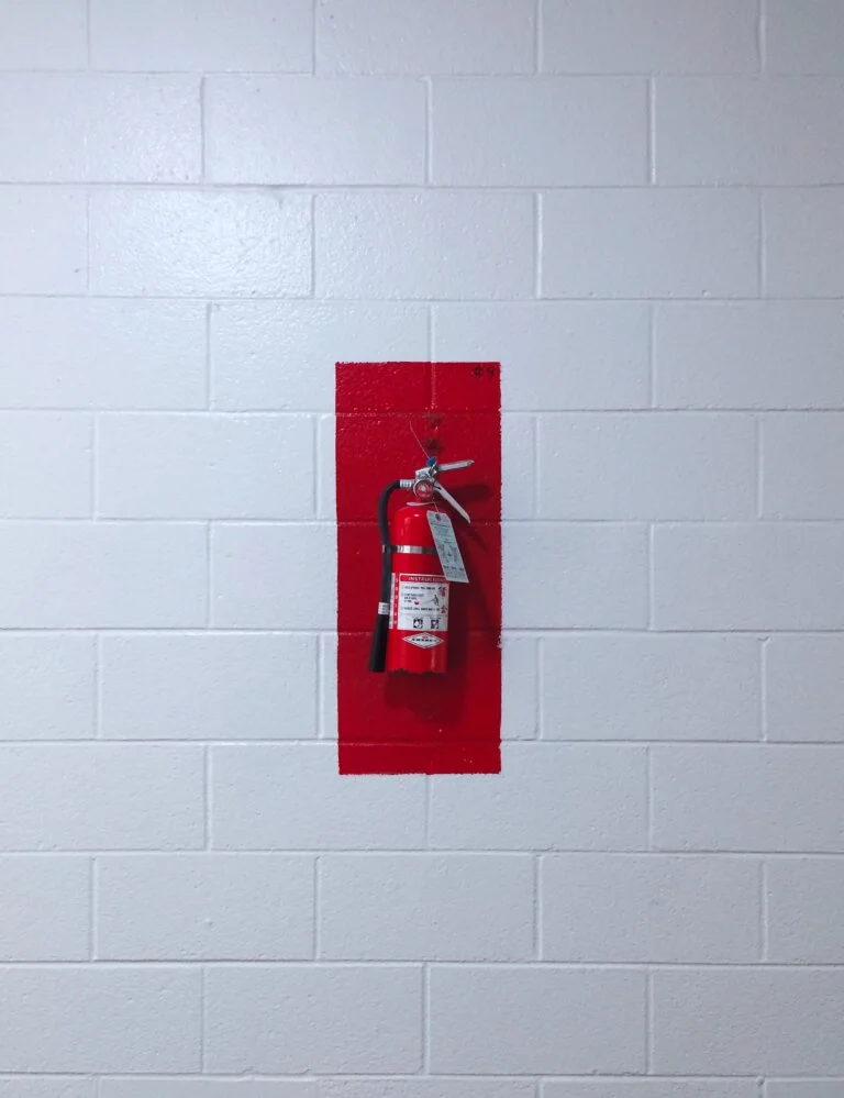 A red fire extinguisher is mounted on a white brick wall.