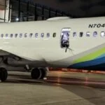 The side of a parked airplane at night with a person standing in the open emergency exit.