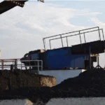 Large piles of compost are next to heavy industrial machinery under a cloudy sky.