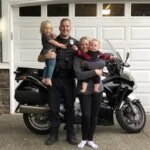 "Police officer and family posing in front of house with motorcycle in driveway"