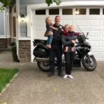"Police officer and family posing in front of house with motorcycle in driveway"