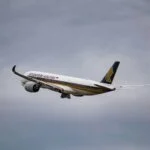 A Singapore Airlines passenger jet in flight, climbing through a cloudy sky.