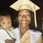 A smiling mother in a graduation cap and gown proudly holds her baby.