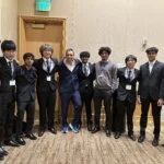 "Group photo of students in suits with speaker at a conference event."