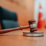 Close-up of a judge’s gavel resting on a sound block in a courtroom.