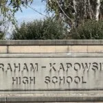 Stone sign reading 'GRAHAM-KAPOWSIN HIGH SCHOOL' surrounded by trees and bushes.
