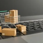Mini shopping cart with cardboard boxes on a laptop keyboard, symbolizing online shopping and e-commerce.