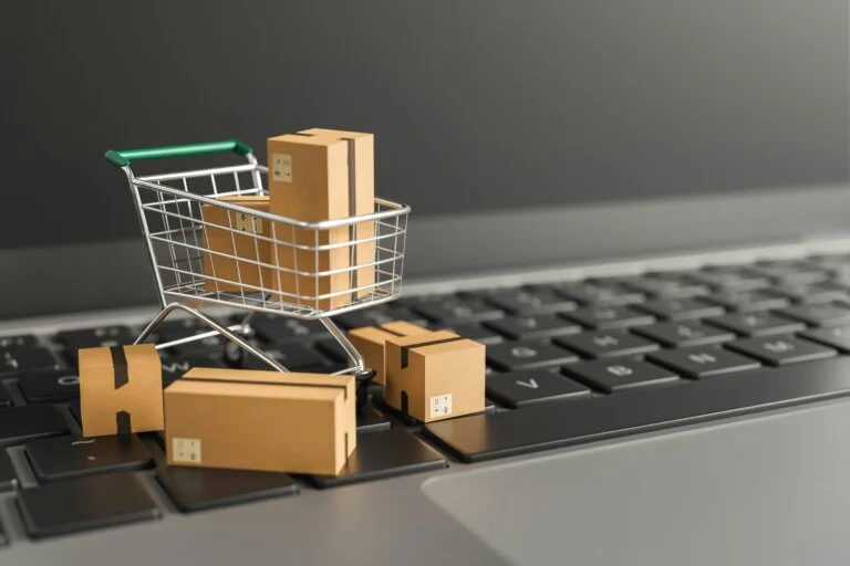 Mini shopping cart with cardboard boxes on a laptop keyboard, symbolizing online shopping and e-commerce.