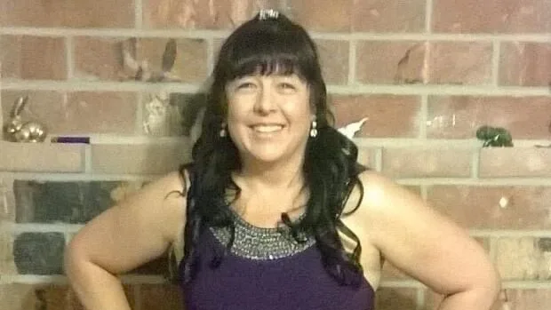 Karin Riebe standing in front of a brick fireplace, smiling and dressed in a purple gown.