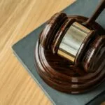 Close-up of a wooden judge’s gavel resting on a sound block atop a closed law book, symbolizing justice and legal proceedings