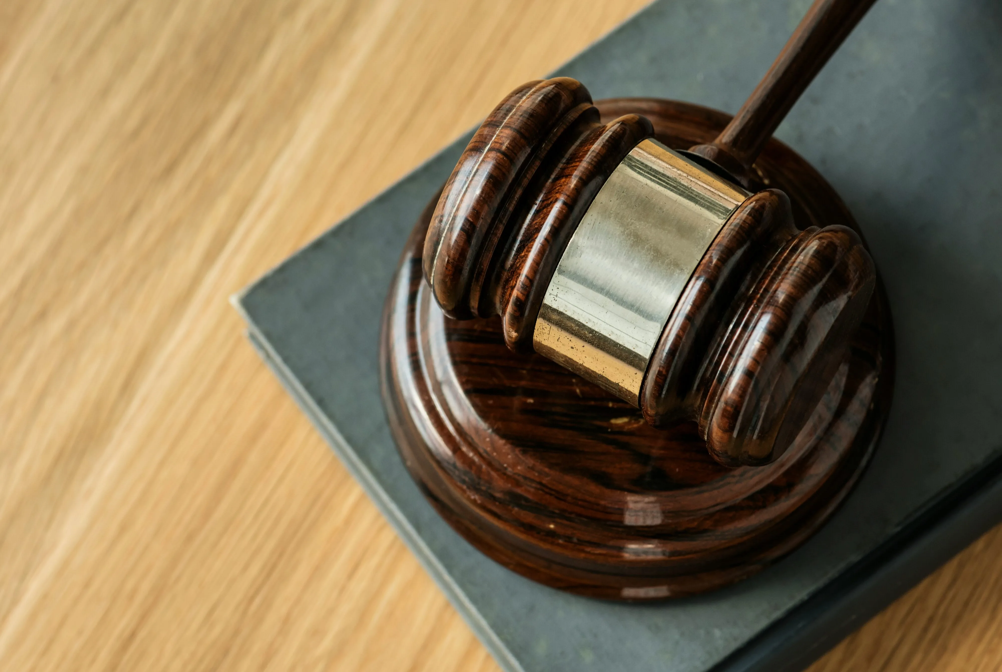 Close-up of a wooden judge’s gavel resting on a sound block atop a closed law book, symbolizing justice and legal proceedings