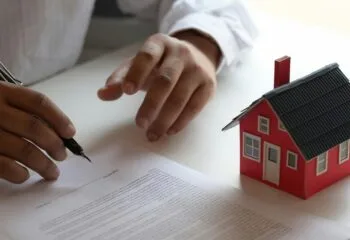 Person reviewing and signing a contract next to a model red house representing a real estate transaction or consumer dispute